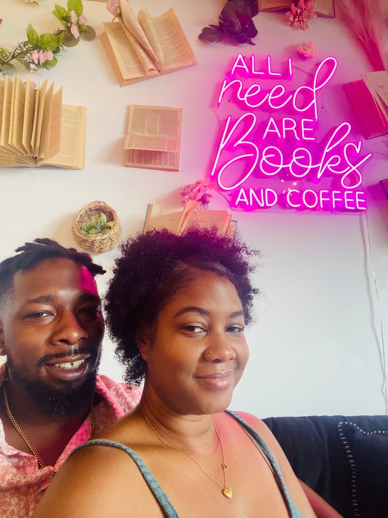 Fallon and her husband under a neon sign reading All I need are books and coffee